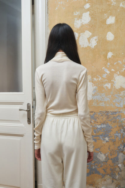 Bea highneck blouse with turtleneck and long sleeves. Cream coloured organic cotton and modal rib. Backside view.