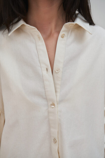 Eba shirt organic cotton shirt with gathered details on the sleeves and body. Ecru unbleached color. Closeup of mother of pearl buttons.