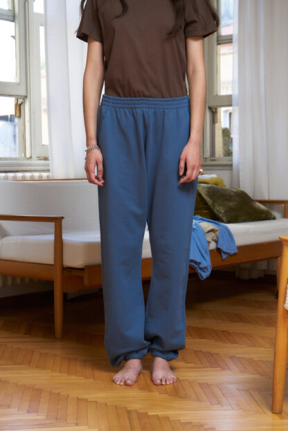 Sea (blue) coloured sweatpants with loose fit and elastic waist. two front pockets. Model is turned away from the camera to show backside.